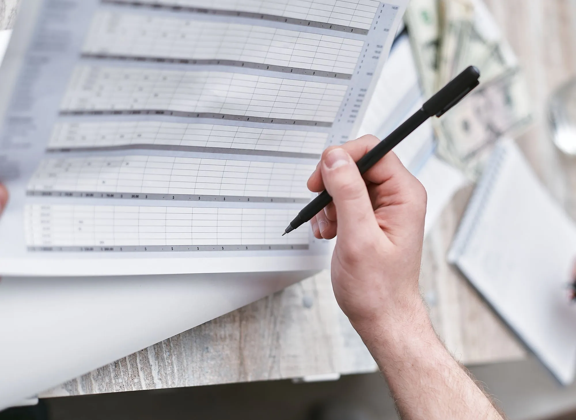 A person holding a pen over a printed spreadsheet.